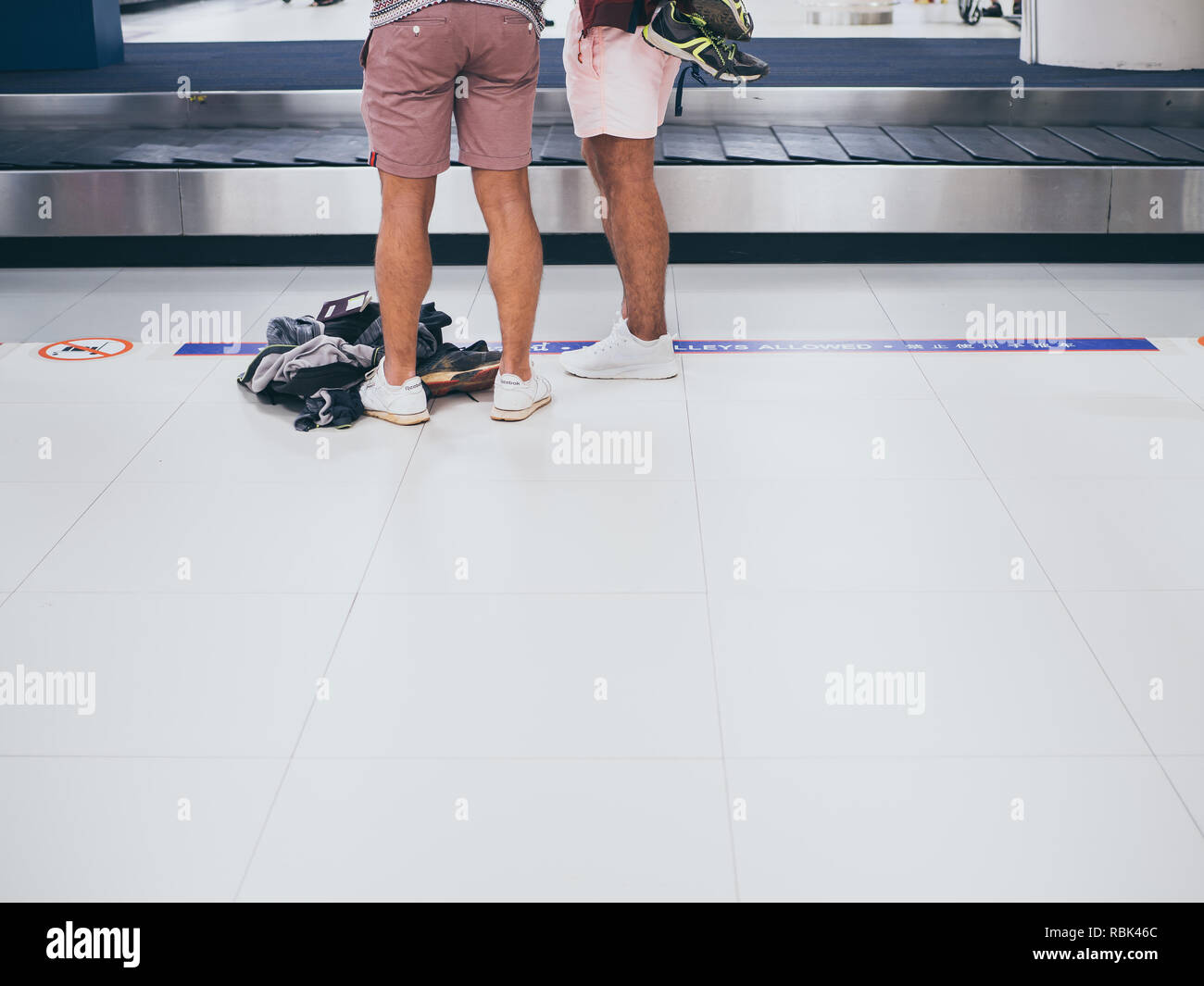 BANGKOK, THAILAND-November 5, 2018: Two tourists wearing shorts and sneakers waiting luggages at the baggage claim in Don Muang International airport  Stock Photo