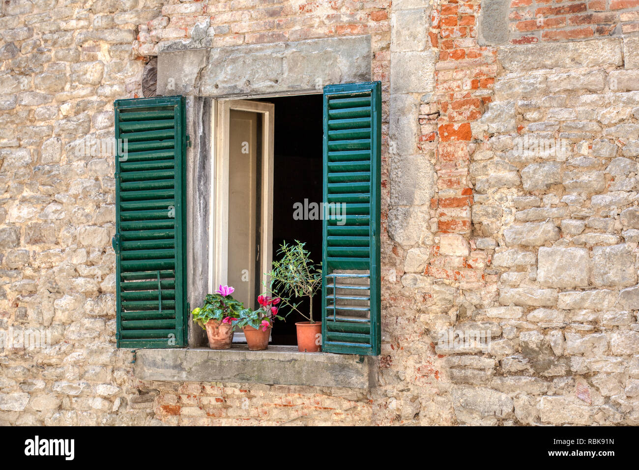 Photograph was taken of a rustic, weathered window with faded green wood shutters in the village of Cortona, Italy located in the heart of Tuscany. Stock Photo