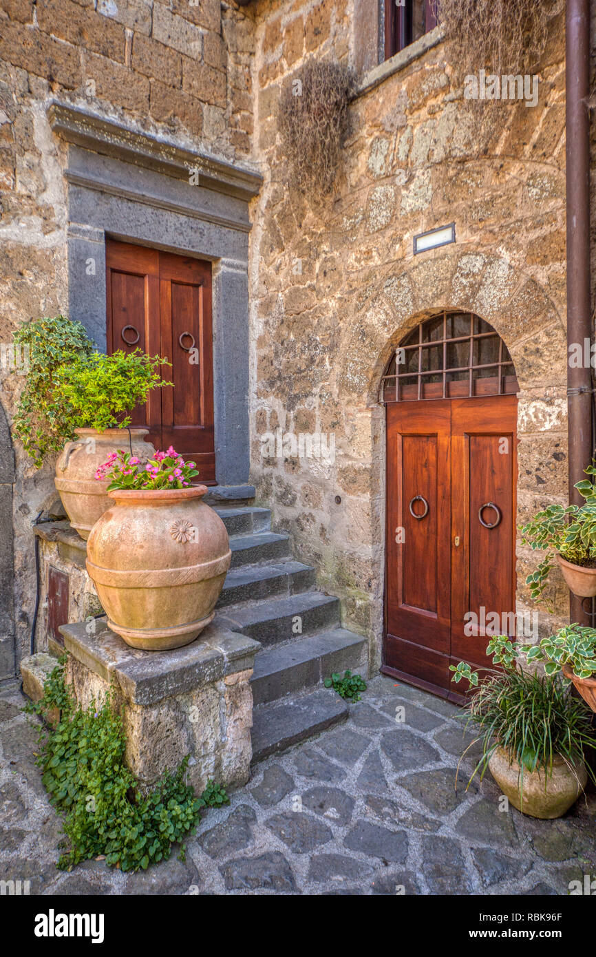 Photograph taken of a romantic, private courtyard of Tuscany. Flowers are flowing from clay vases with weatered wood medieval doors. Stock Photo
