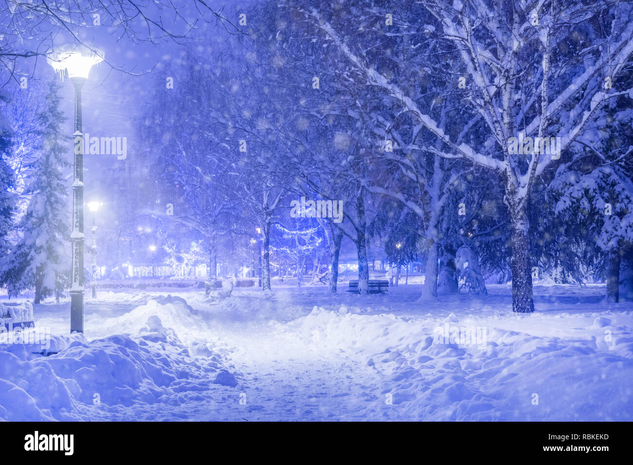 Winter idyll park in the night and footpath covered with big snow. Shining lantern through snowing in the evening. Its snowing and cold winter weather Stock Photo