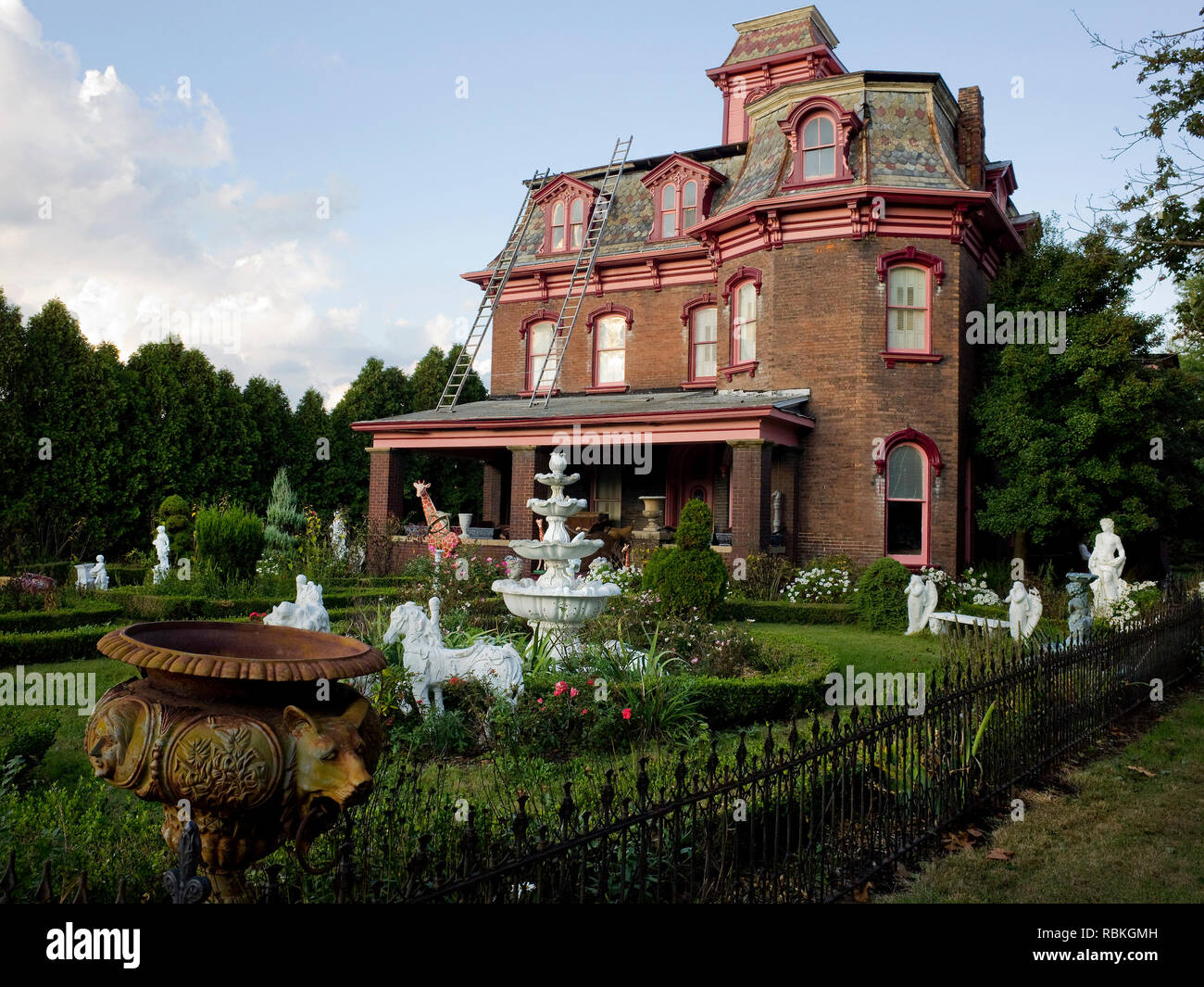 An old Victorian brick house with a fantasy garden of statues and flowers in the yard. Stock Photo
