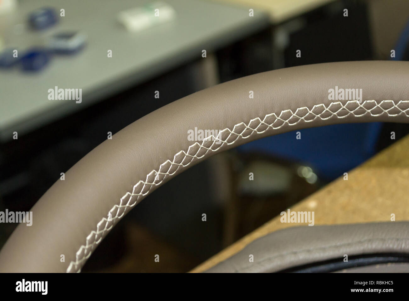 Leather steering wheel beige color stitched again with a bright contrast seam in the workshop for the repair of car interiors and tuning design Stock Photo