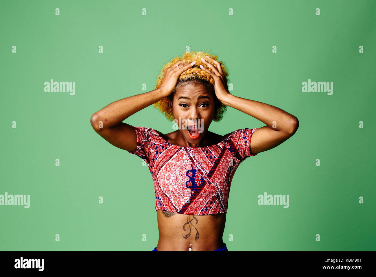 Young woman holding her head with mouth open in disbelief and shock, isolated on green studio background Stock Photo
