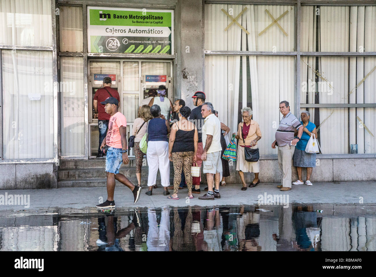 diverse multiracial group of Cuban people wait in line to use sidewalk cash machines of Banco Metropolitano in Havana which dispense only Cuban pesos Stock Photo