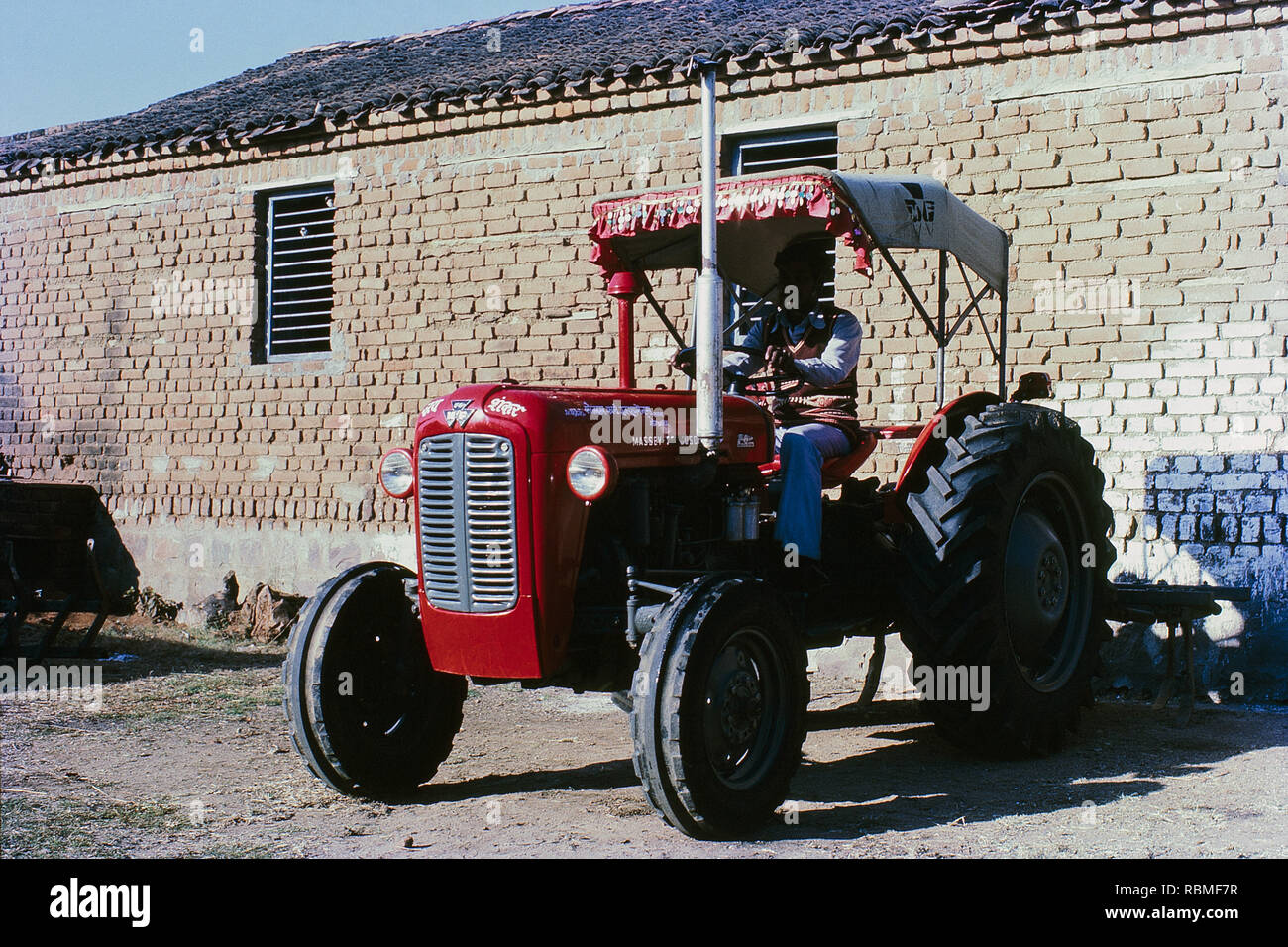 Red colour tractor parked in front of brick wall, India, Asia Stock Photo