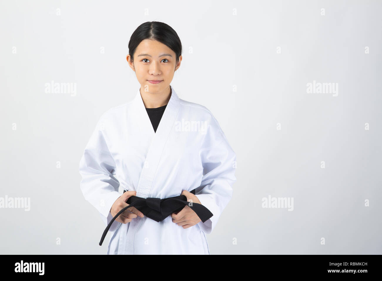 Young beautiful woman wearing karate suit holding black belt on white background Stock Photo