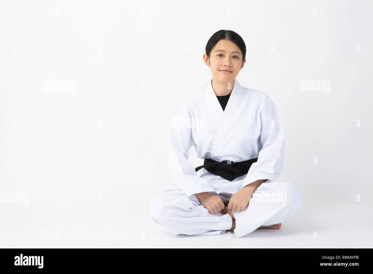 Young beautiful woman wearing karate suit sitting and smiling on white background Stock Photo