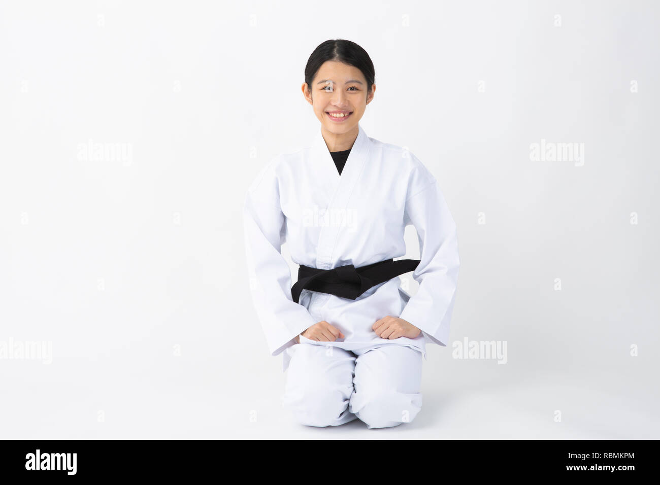 Young beautiful woman wearing karate suit sitting and smiling on white background Stock Photo