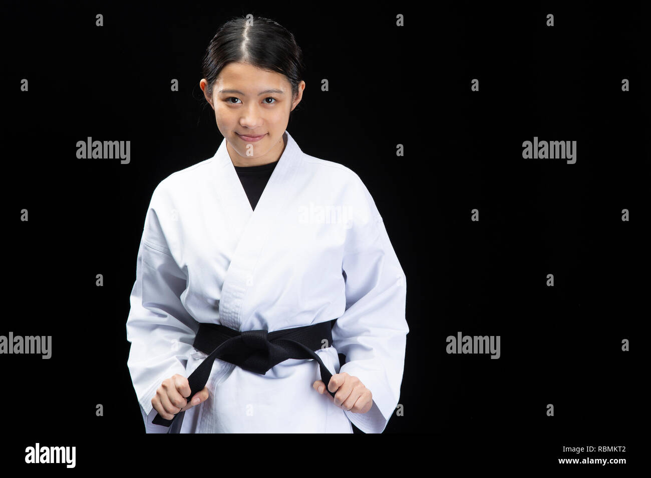 Young beautiful woman wearing karate suit holding black belt and smiling on black background Stock Photo