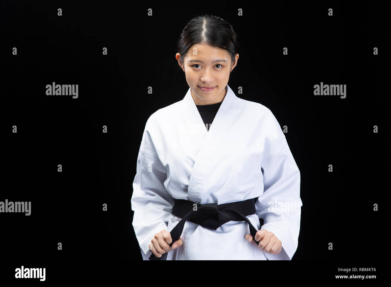 Young beautiful woman wearing karate suit holding black belt and smiling on black background Stock Photo