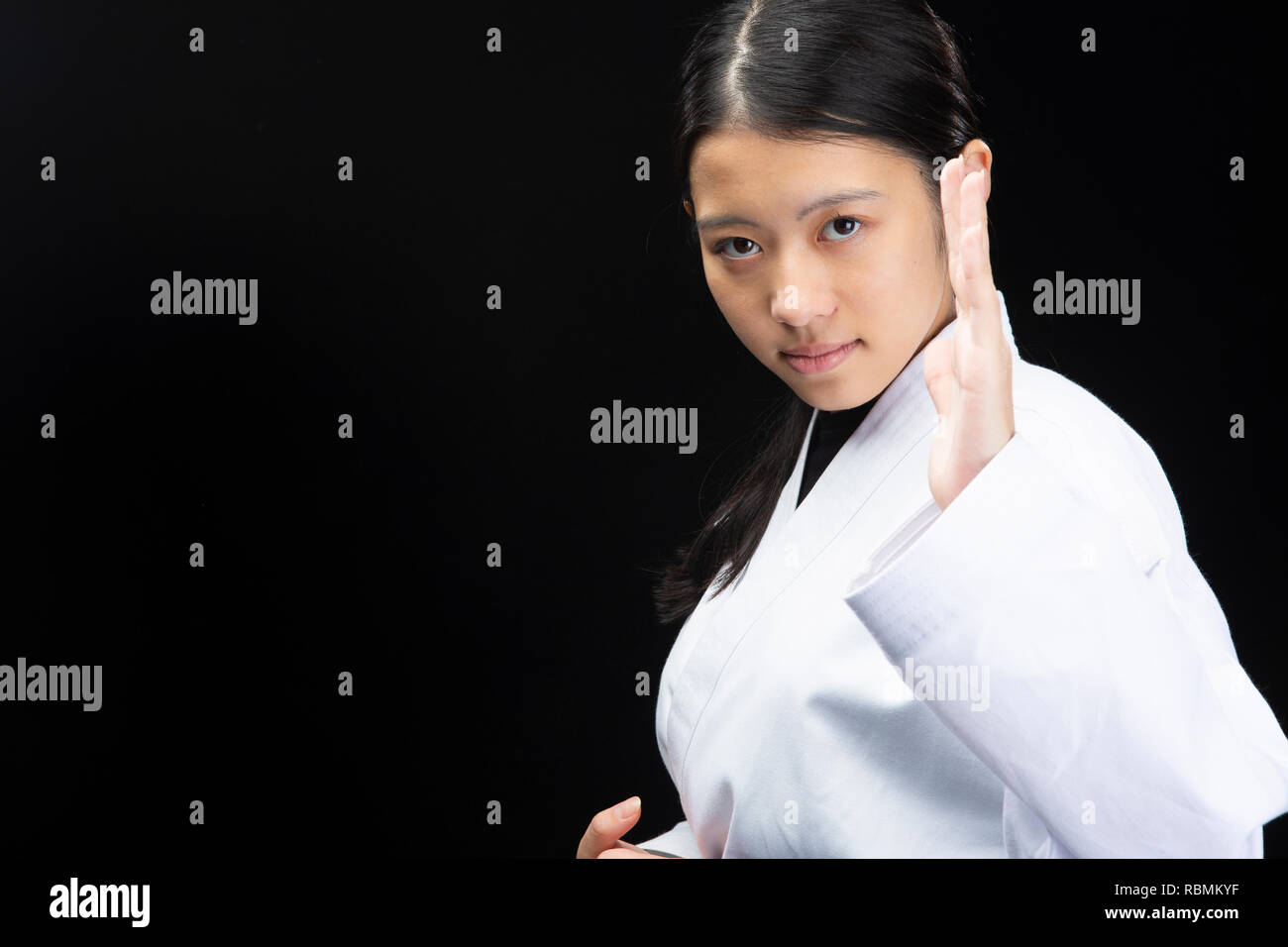 Young beautiful woman wearing a karate suit performing Karate on black
