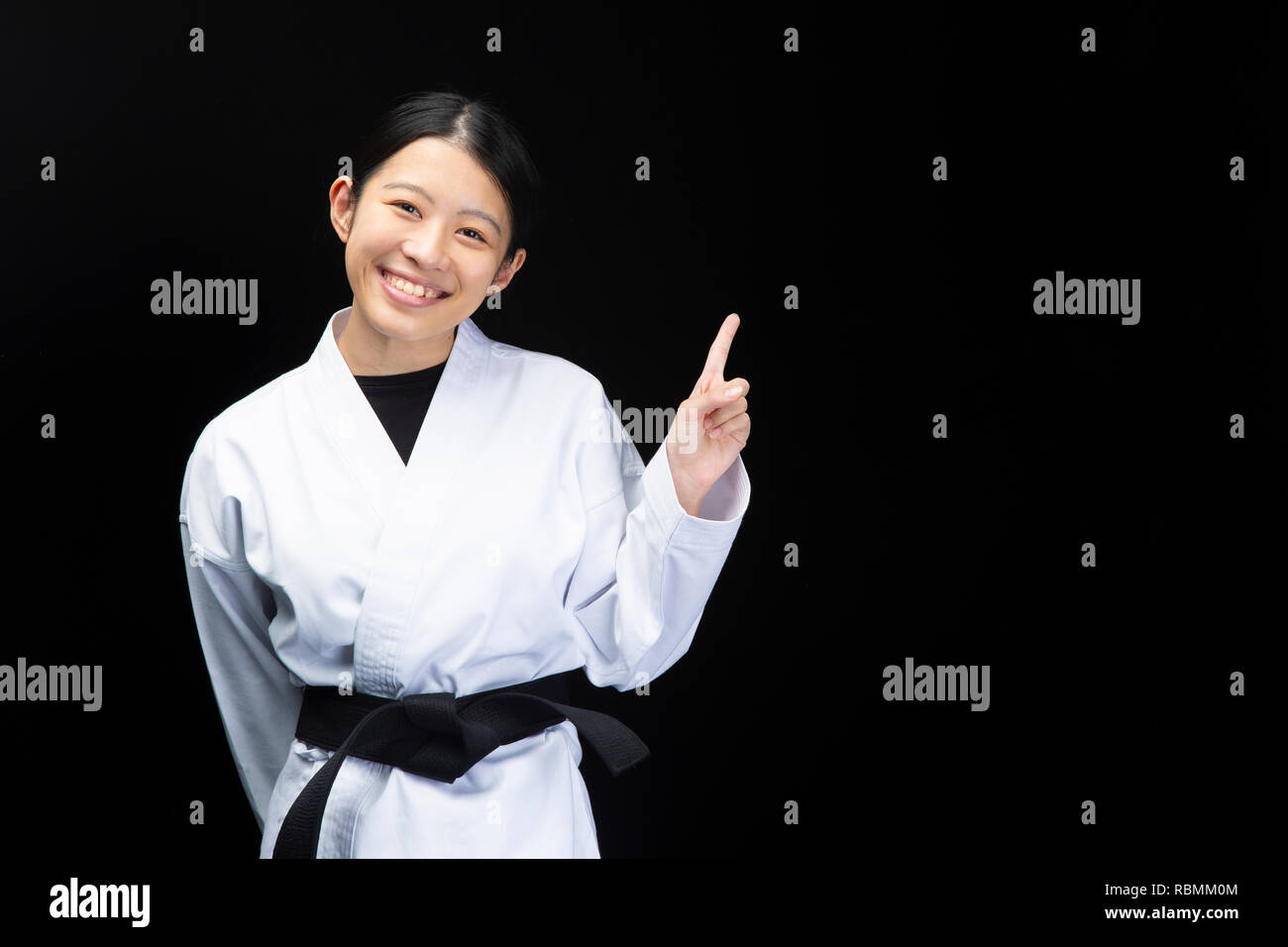 Woman in a karate suit pointing with fingers on black background Stock Photo