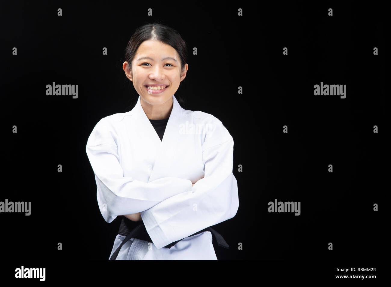 Young woman in Karate suit crossing arms with happy face on black