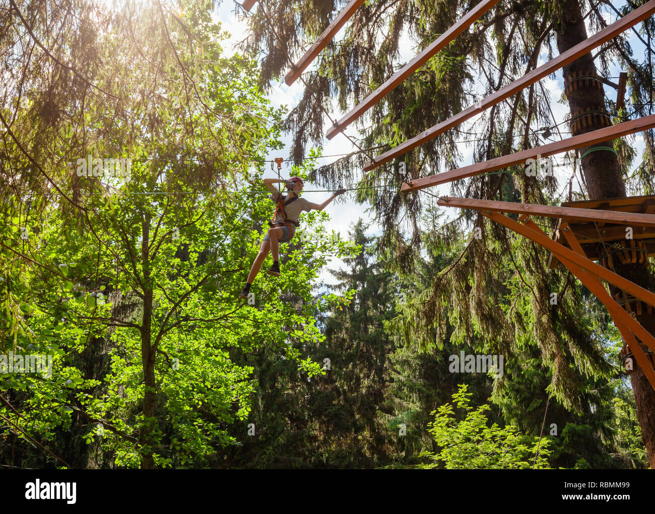 Teenager boy wearing safety harness passing zip line at a ropes course ...