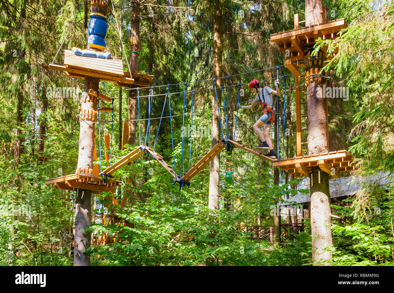 Teenager boy wearing safety harness passing rope bridge obstacle at a ropes course in outdoor treetop adventure park Stock Photo