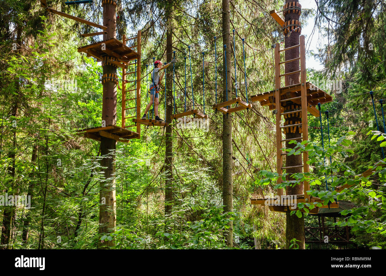 Teenager boy wearing safety harness passing rope bridge obstacle at a ropes course in outdoor treetop adventure park Stock Photo