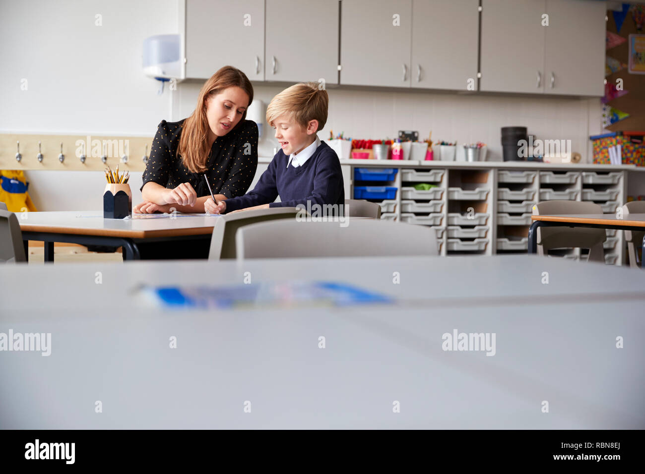 Young female primary school teacher and schoolboy sitting at a table working one on one, selective focus Stock Photo