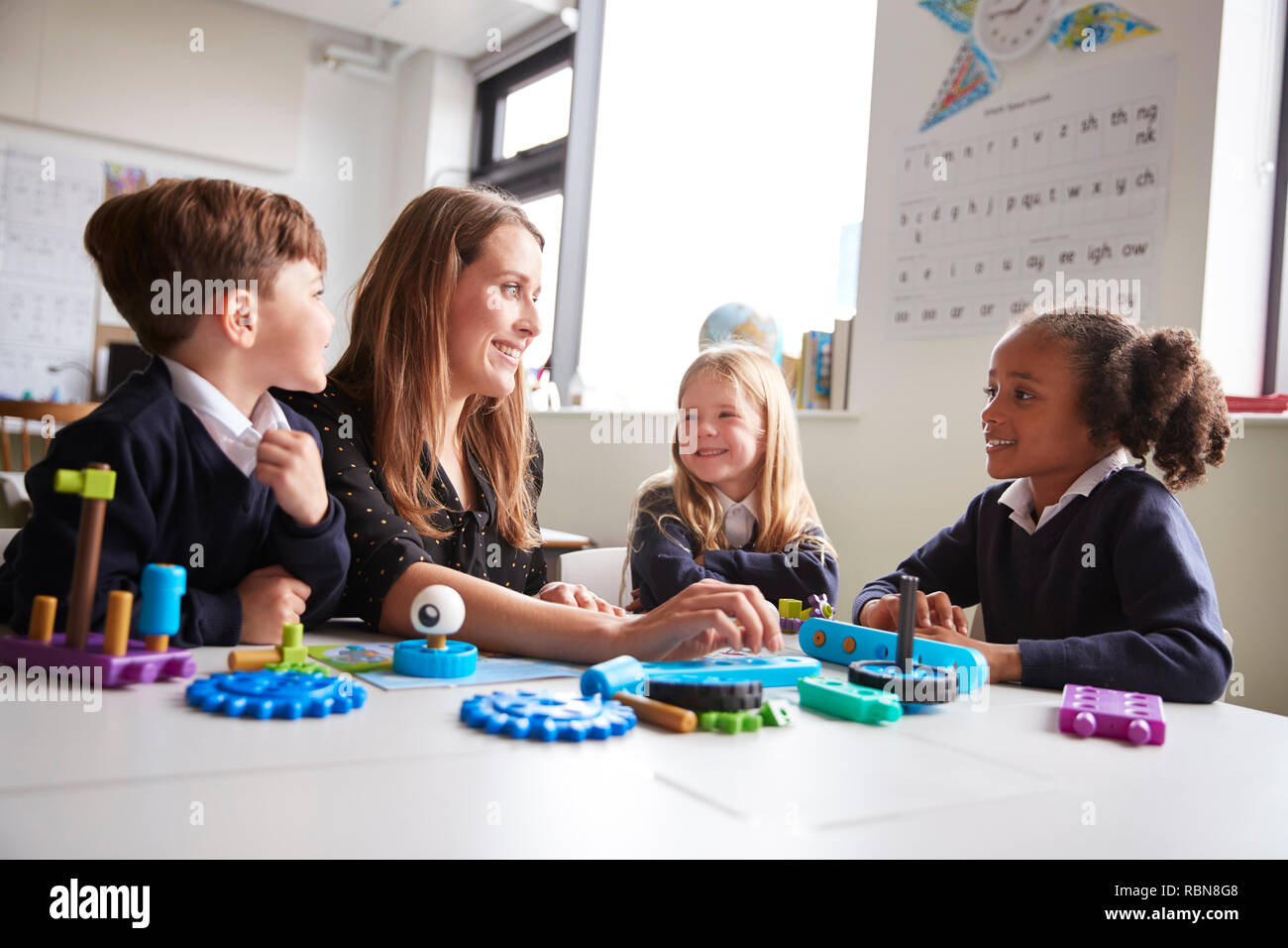 Female teacher and three primary school kids sitting at a table in a classroom working with educational construction toys, close up, low angle Stock Photo