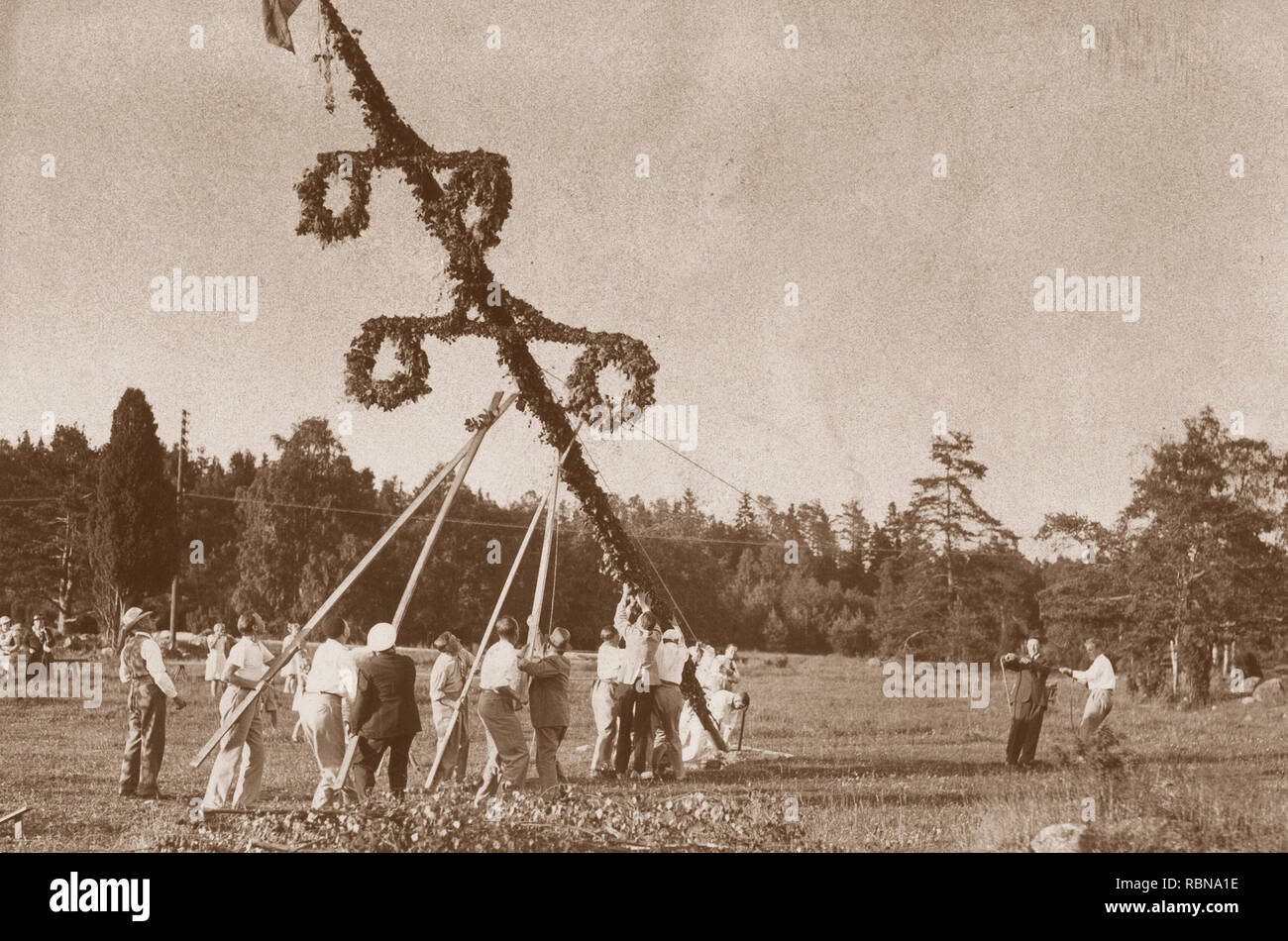 Midsummer tradition in the 1930s. As a part of the festivities a Maypole is risen and here a group of people rises the pole before beginning to dance around it. Sweden 1930s. Stock Photo