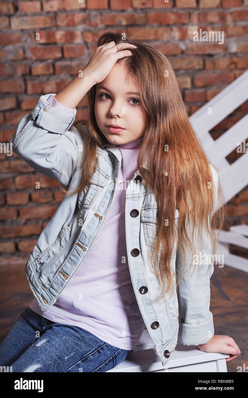 Portrait little fashion kid.Stylish hipster girl child wearing denim jacket,jeans clothes,posing against rough brick wall. looks confident,defiant.Beautiful face caucasian Children's,fashion concept. Stock Photo