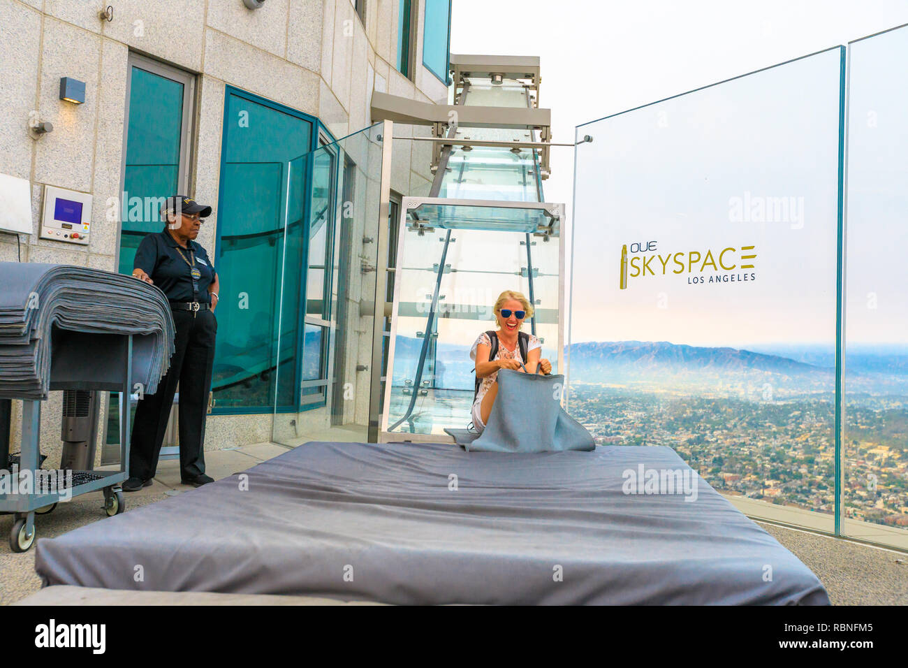 Los Angeles, California, United States - August 9, 2018: the experience of funny tourist woman riding on the Skyslide all-glass at popular US Bank Tower with open-air terrace over the downtown LA. Stock Photo