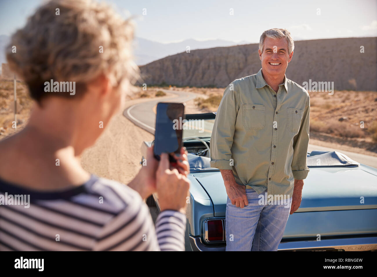 Wife taking shot of her husband on road trip with smartphone Stock Photo