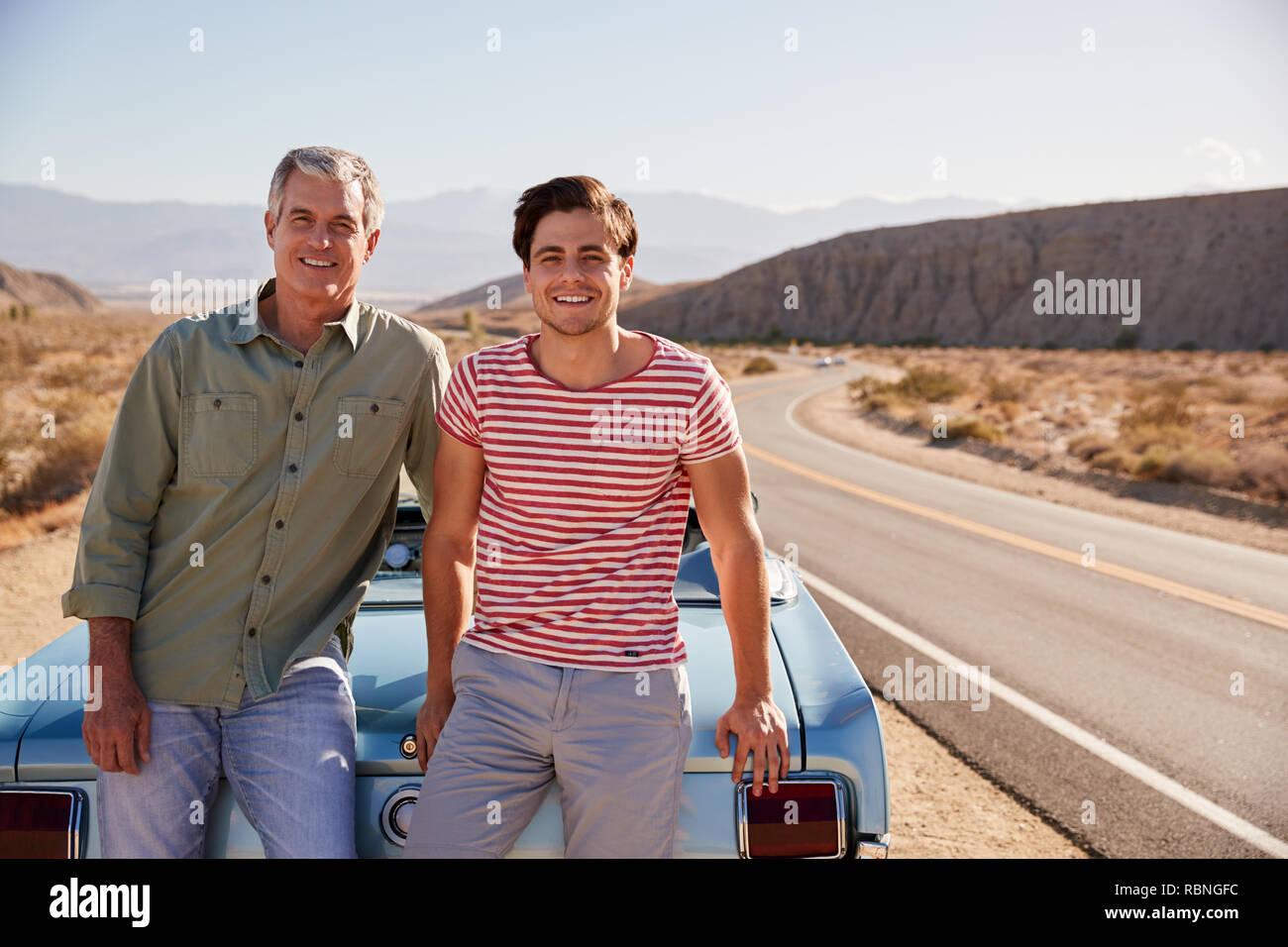 Father and adult son on road trip leaning against their car Stock Photo
