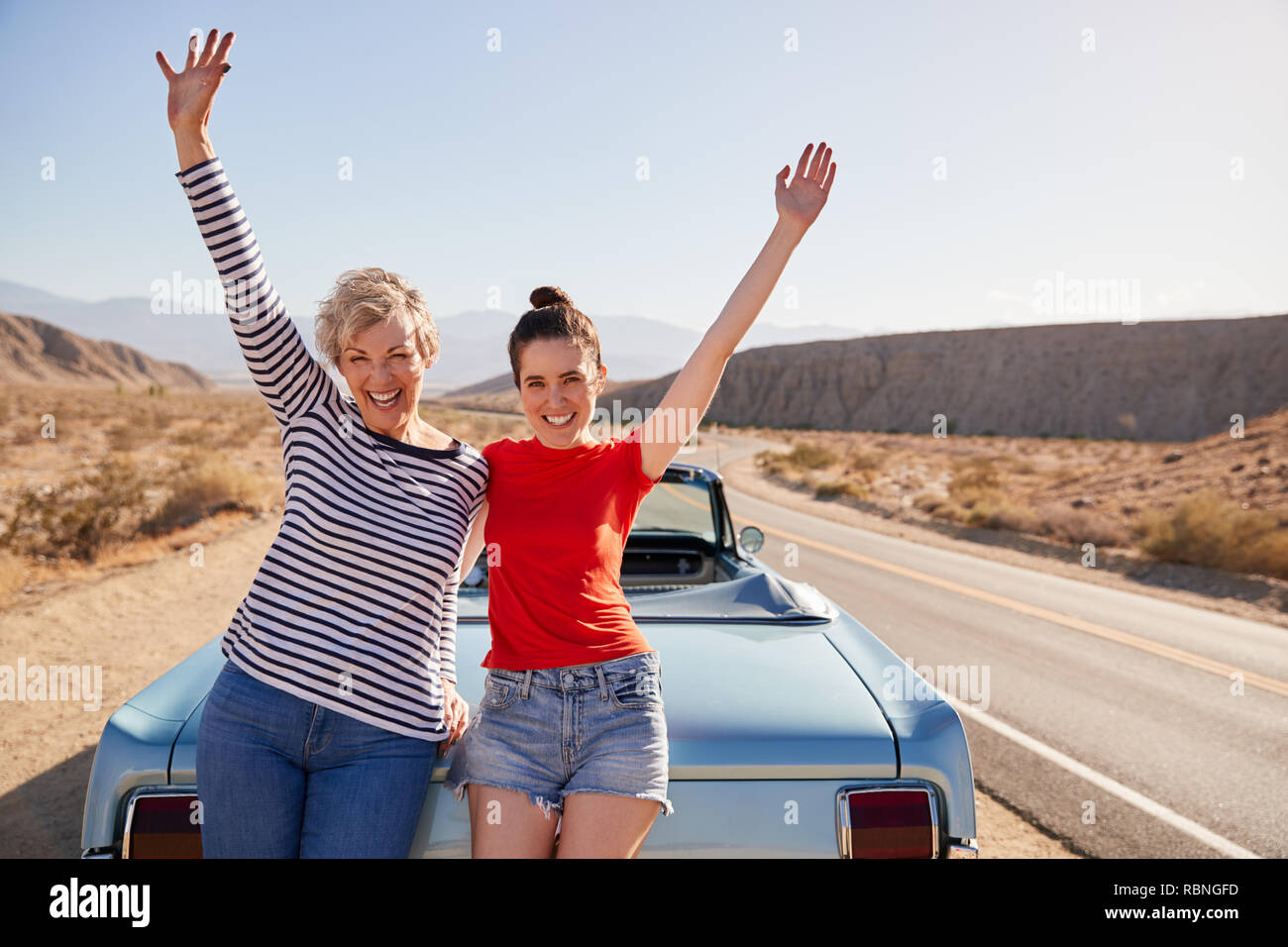 Mum and adult daughter on road trip stand waving to camera Stock Photo