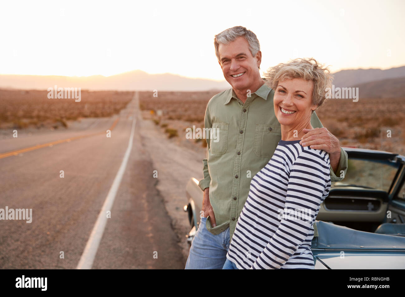 Senior couple on road trip standing by car smiling to camera Stock Photo