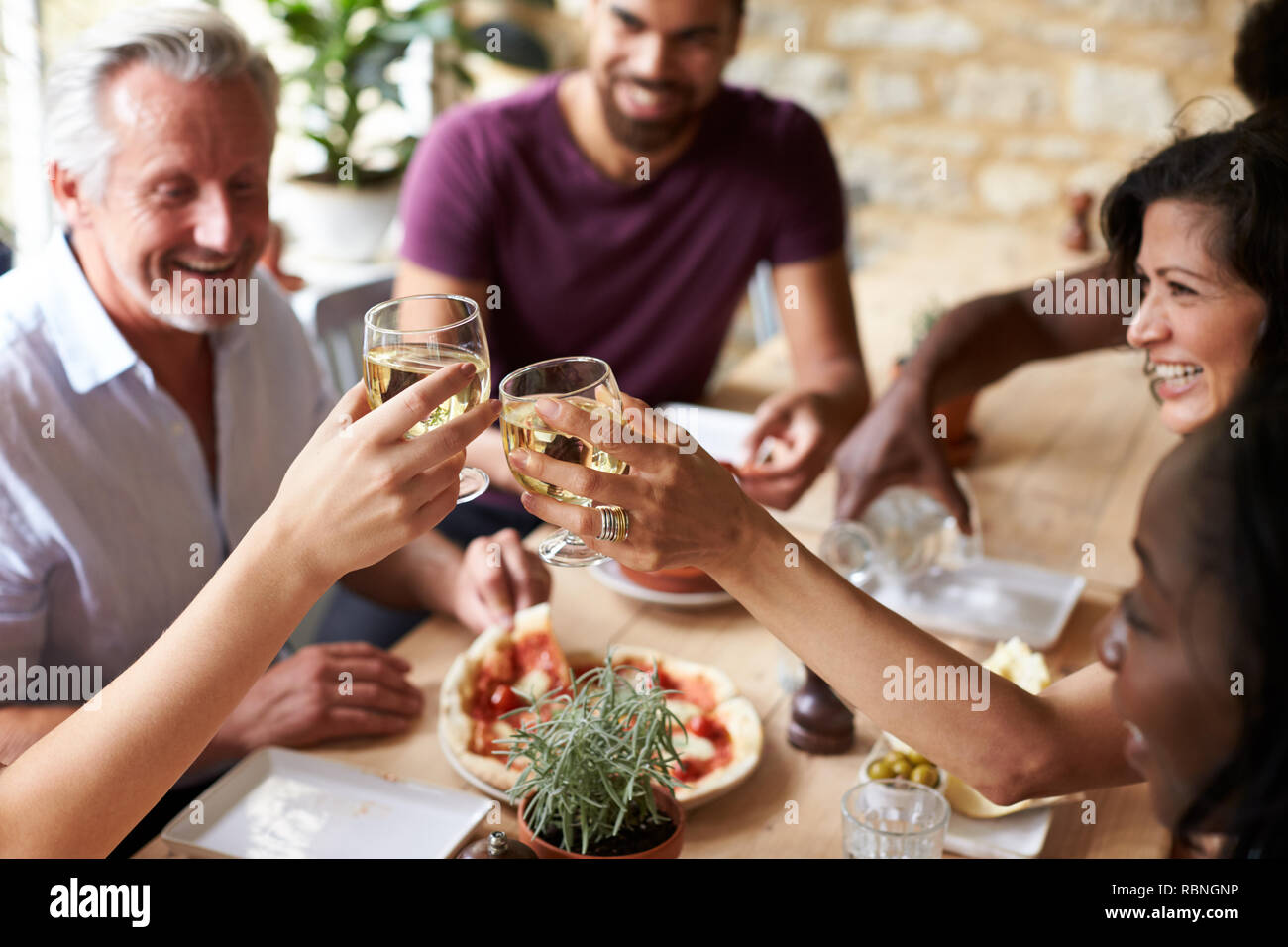Smiling friends eating at a table in a cafe making a toast Stock Photo