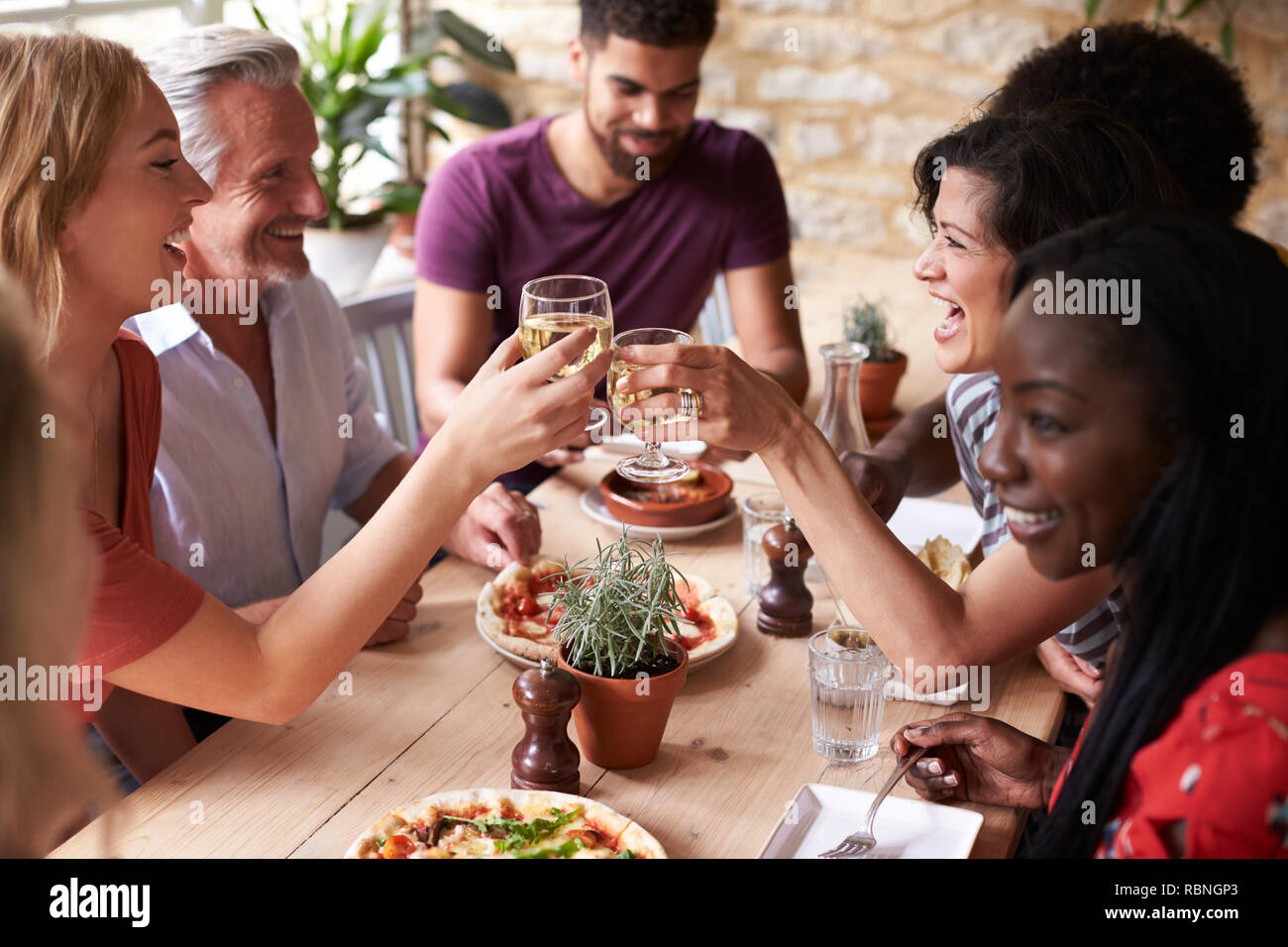Friends laughing at a dining table in a cafe making a toast Stock Photo