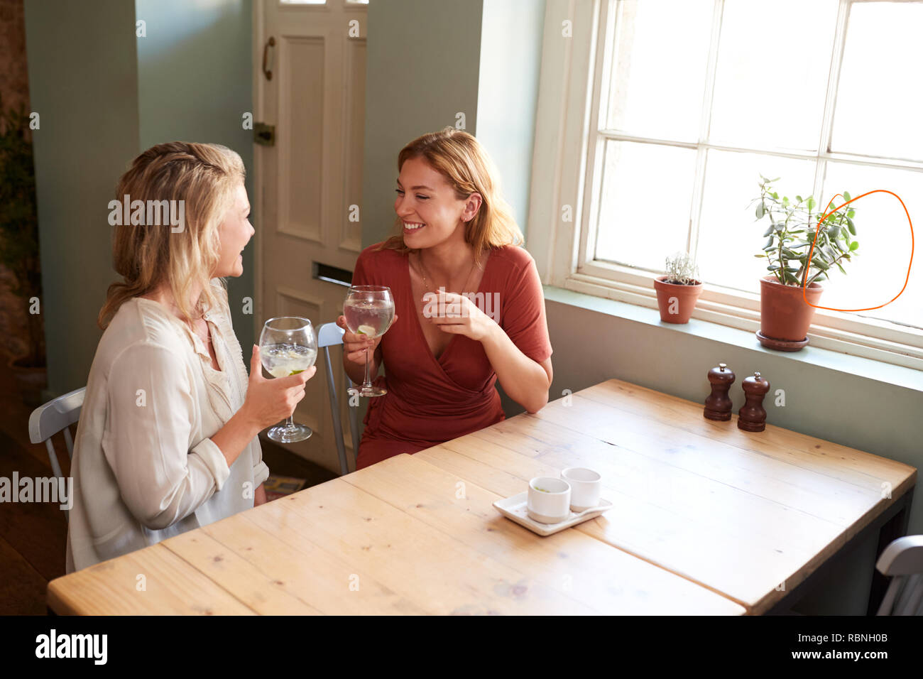 Two young female friends talking over drinks in a pub Stock Photo