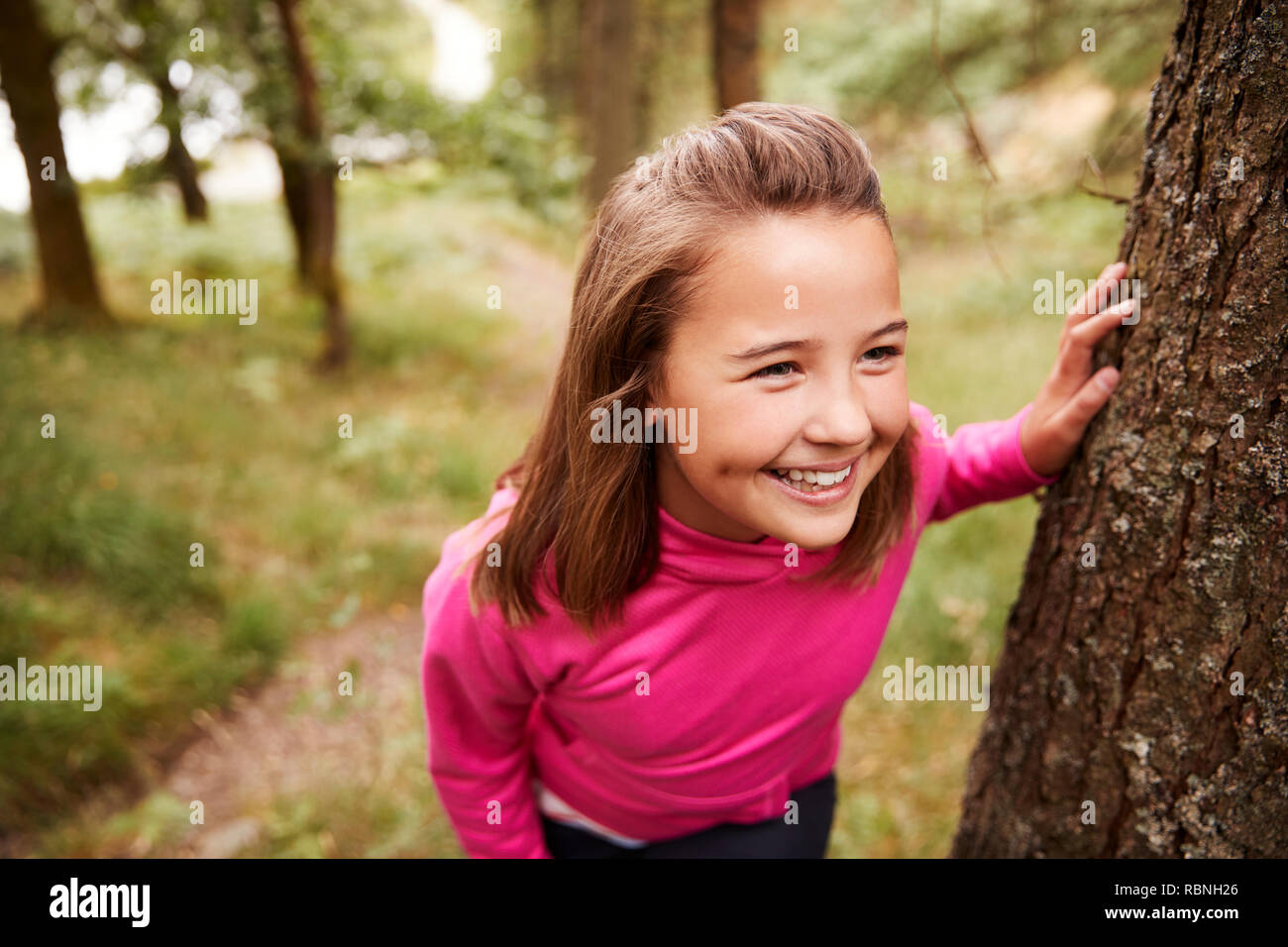 Pre-teen girl taking a break leaning on tree during a hike in a forest, elevated view, close up Stock Photo