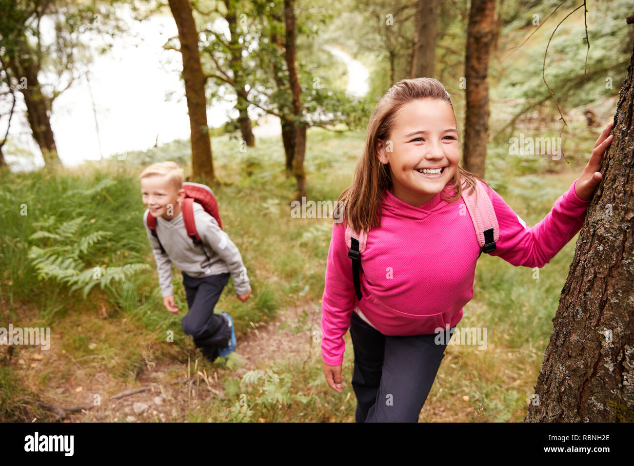 Pre-teen girl taking a break leaning on a tree in a forest, her brother in the background Stock Photo