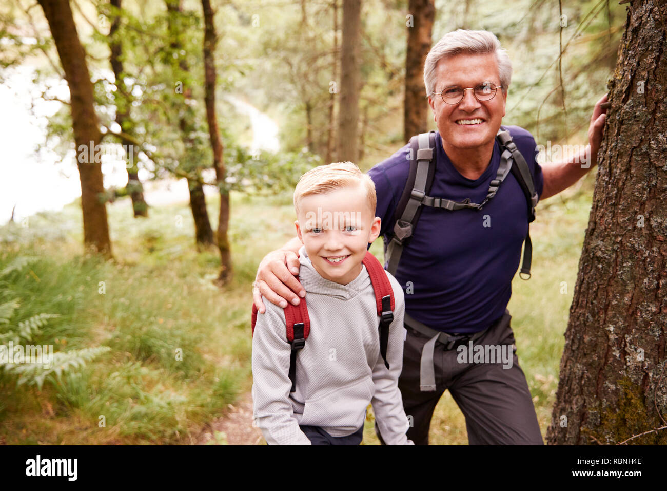 Grandfather and grandson taking a break while hiking together in a forest, close up, smiling to camera Stock Photo