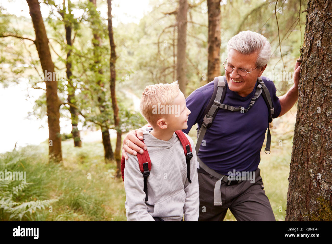 Grandfather and grandson taking a break while hiking together in a forest, close up, looking at each other Stock Photo