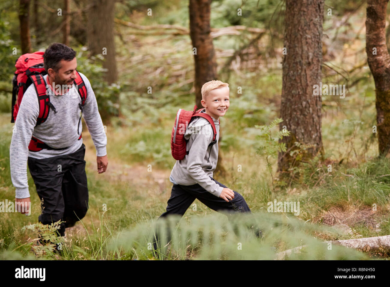 Side view of a boy walking on trail in a forest with his father and looking to camera, selective focus Stock Photo