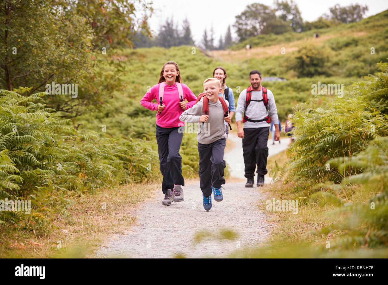 Children running ahead of parents walking on a country path during a family camping trip, selective focus Stock Photo
