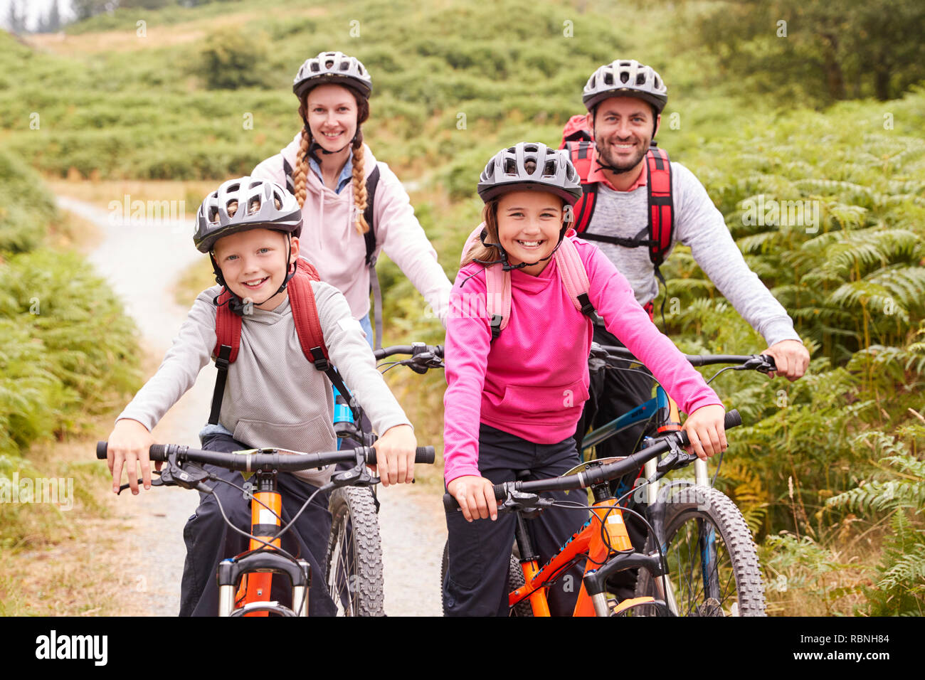 Portrait of parents and children sitting on mountain bikes in a country lane during a family camping trip, front view Stock Photo