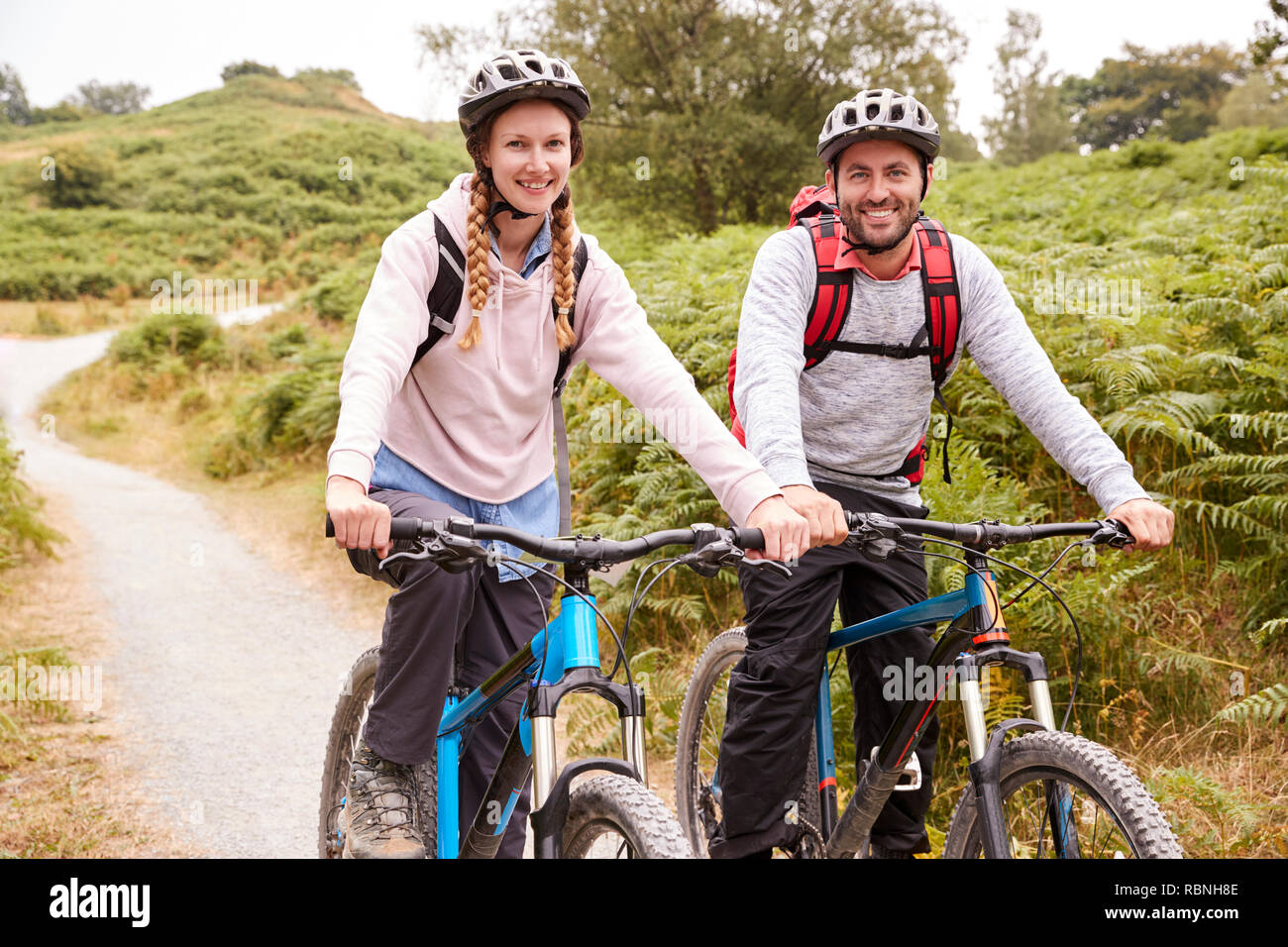 Young adult couple sitting on mountain bikes in a country lane during a camping holiday, close up Stock Photo