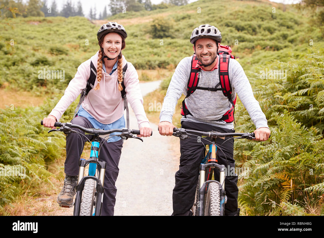 Young adult couple riding mountain bikes in a country lane, looking at camera, close up Stock Photo