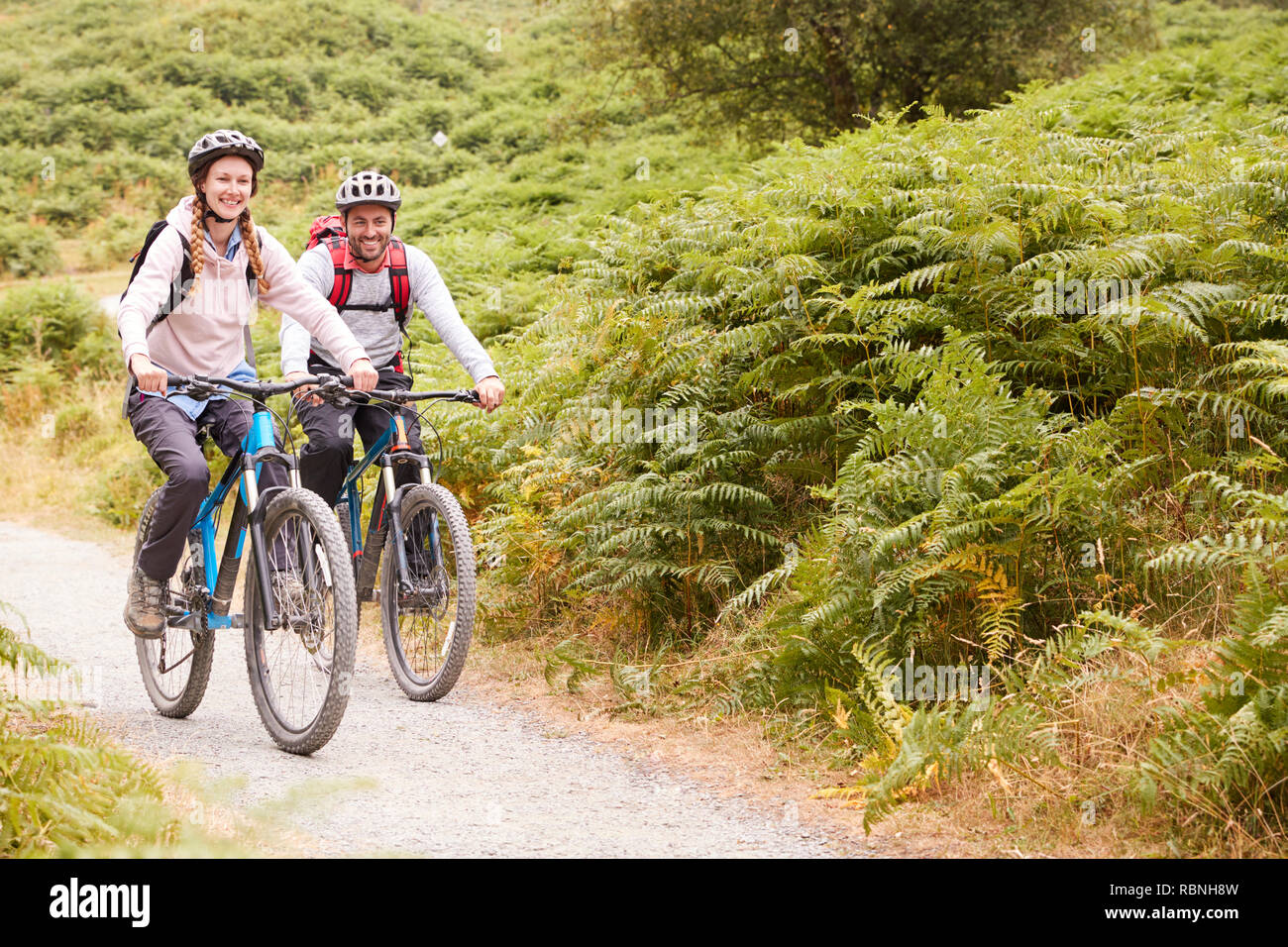 Young adult couple riding mountain bikes in the countryside, full length Stock Photo