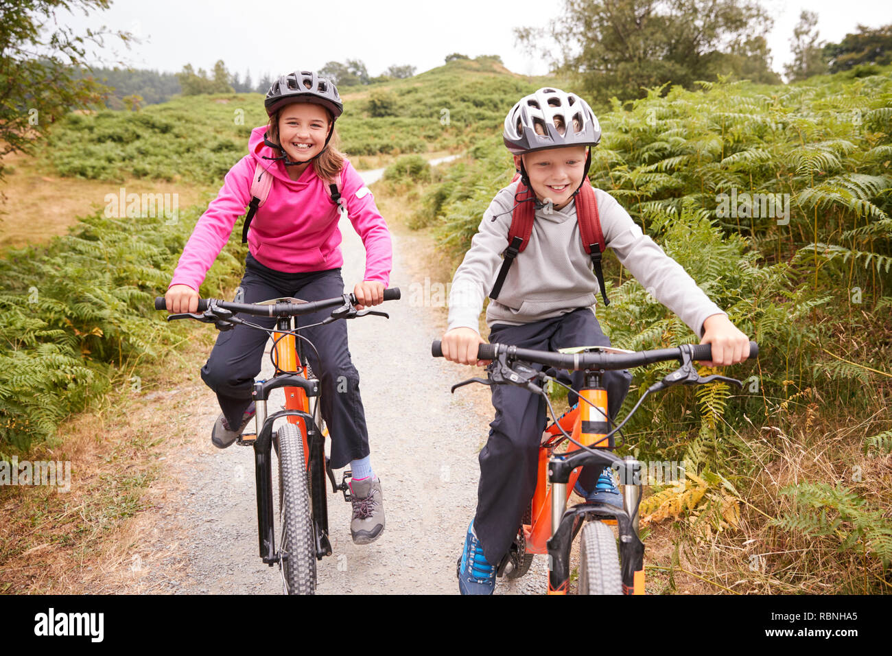 Two children riding mountain bikes on a country path laughing, front view Stock Photo