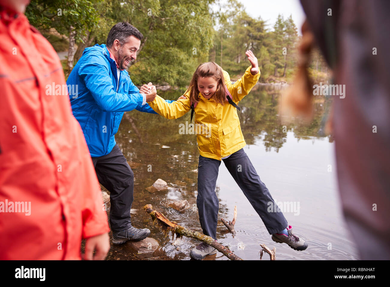 Middle aged father holding his daughter’s hand while she balances on the shore of a lake, Lake District, UK Stock Photo