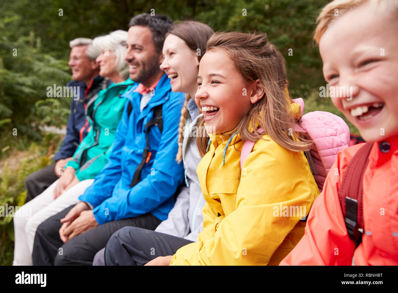 Side view of multi generation family admiring the view sitting together on the shore of a lake laughing, selective focus, Lake District, UK Stock Photo