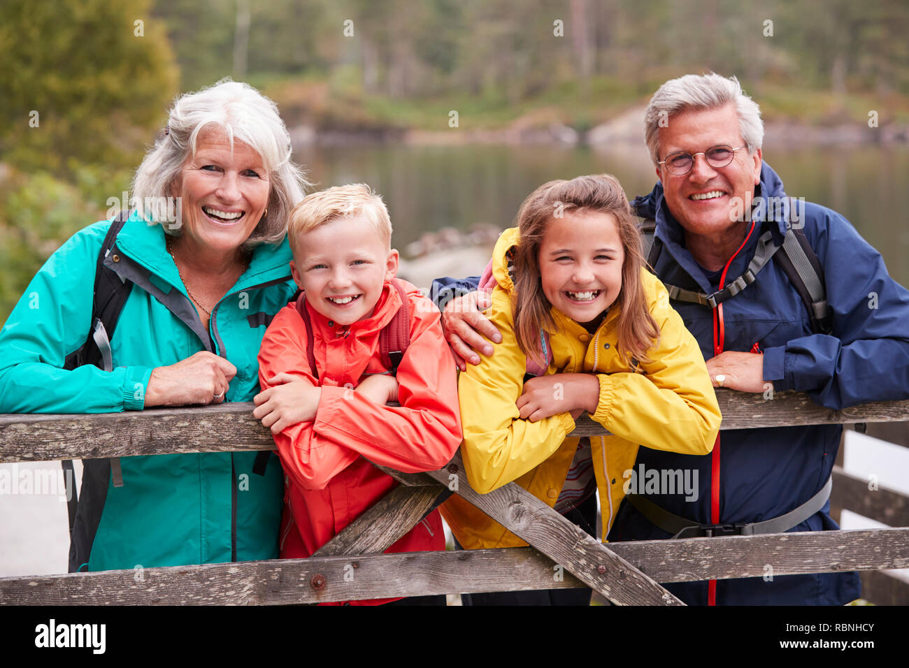 Grandparents and grandchildren leaning on a wooden fence in the countryside laughing, Lake District, UK Stock Photo