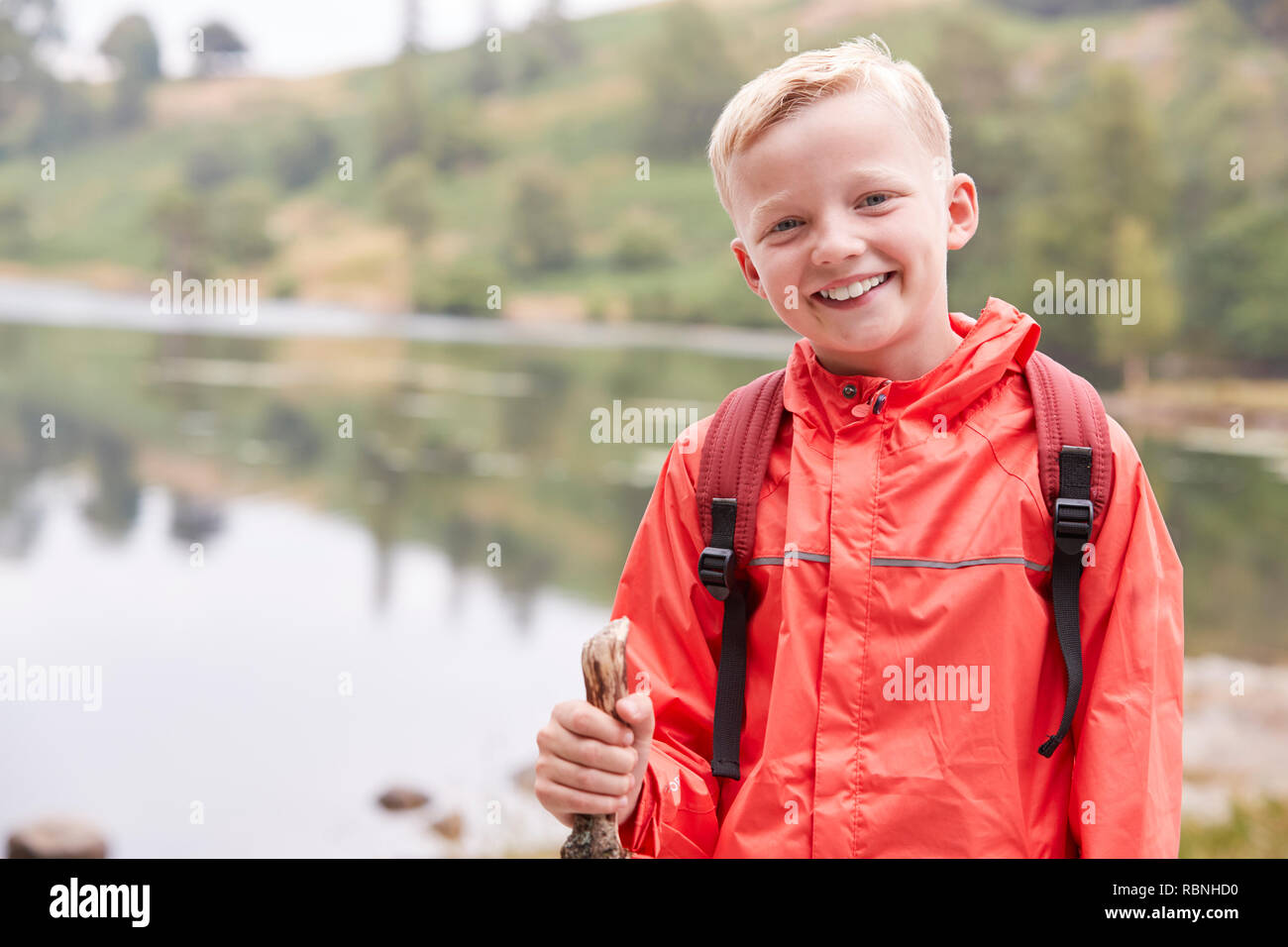 A pre-teen boy standing on the shore of a lake, looking to camera, front view, waist up, Lake District, UK Stock Photo