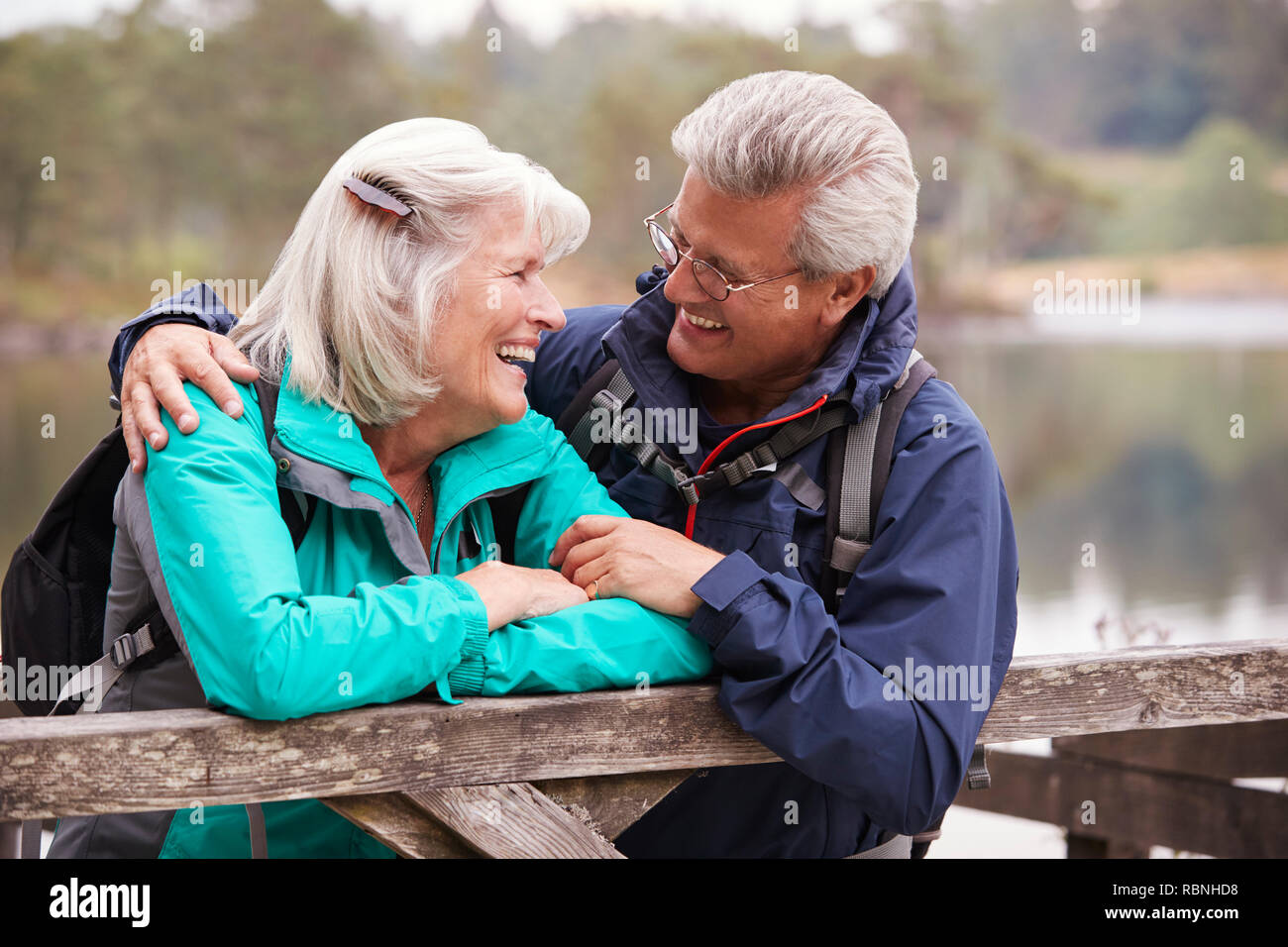Happy senior couple leaning on a wooden fence smiling to each other, close up, Lake District, UK Stock Photo