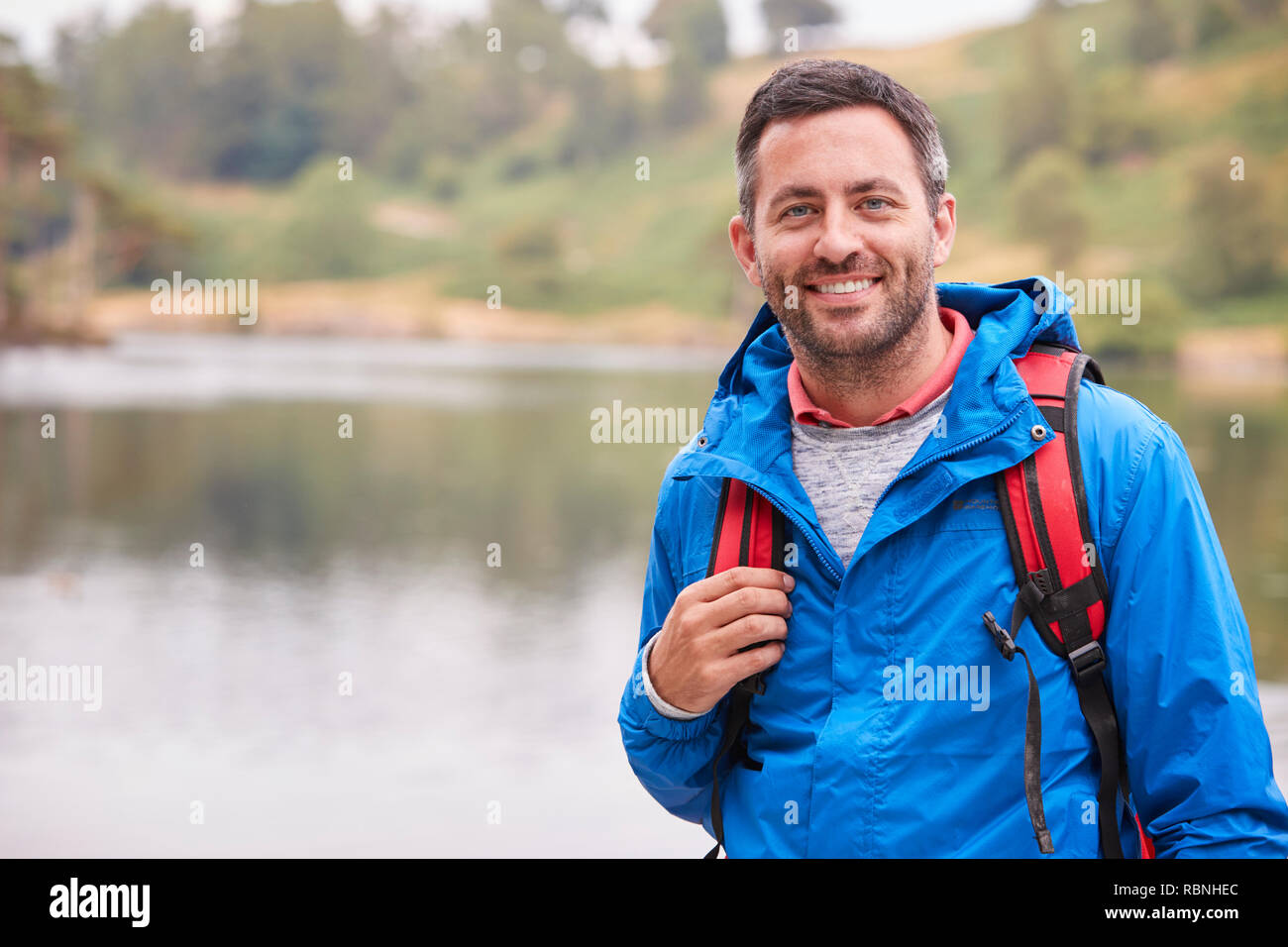 Adult man on a camping holiday standing by a lake smiling to camera, portrait, Lake District, UK Stock Photo