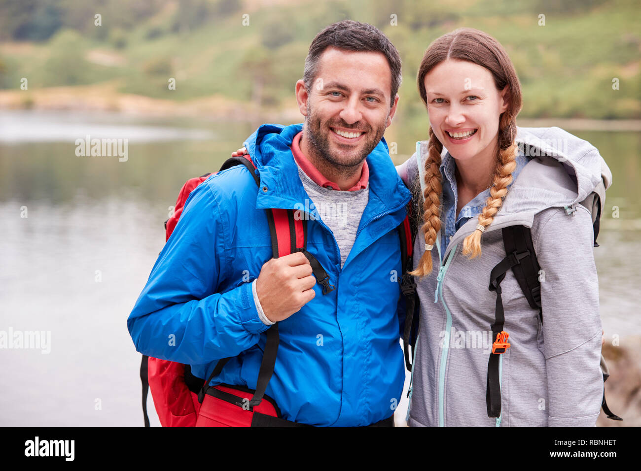Young adult couple on a camping trip standing near a lake looking to camera, close up, Lake District, UK Stock Photo